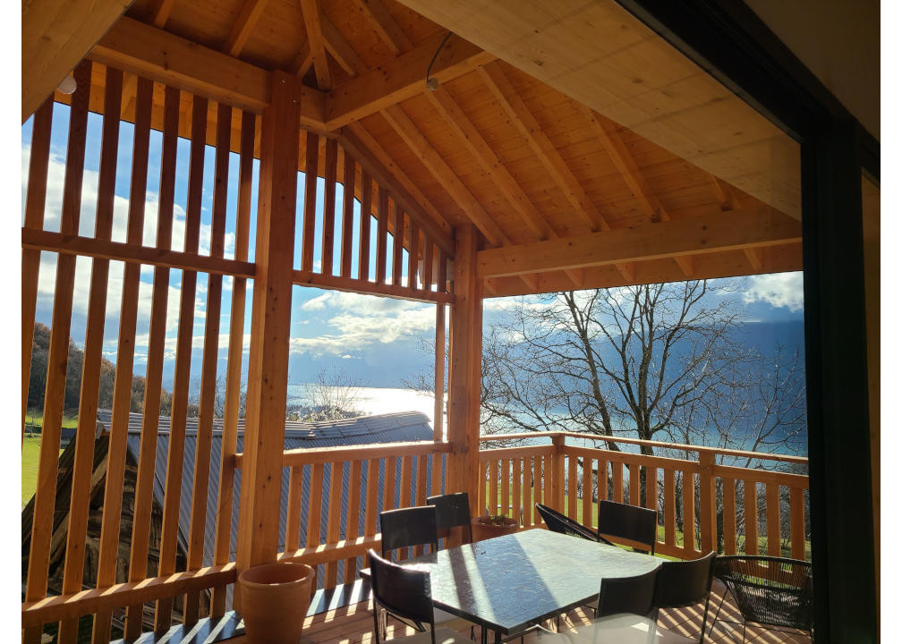 La terrasse d'un gite de groupe en Savoie tout en bois avec une table, 6 chaises et une vue panoramique sur le lac du Bourget.